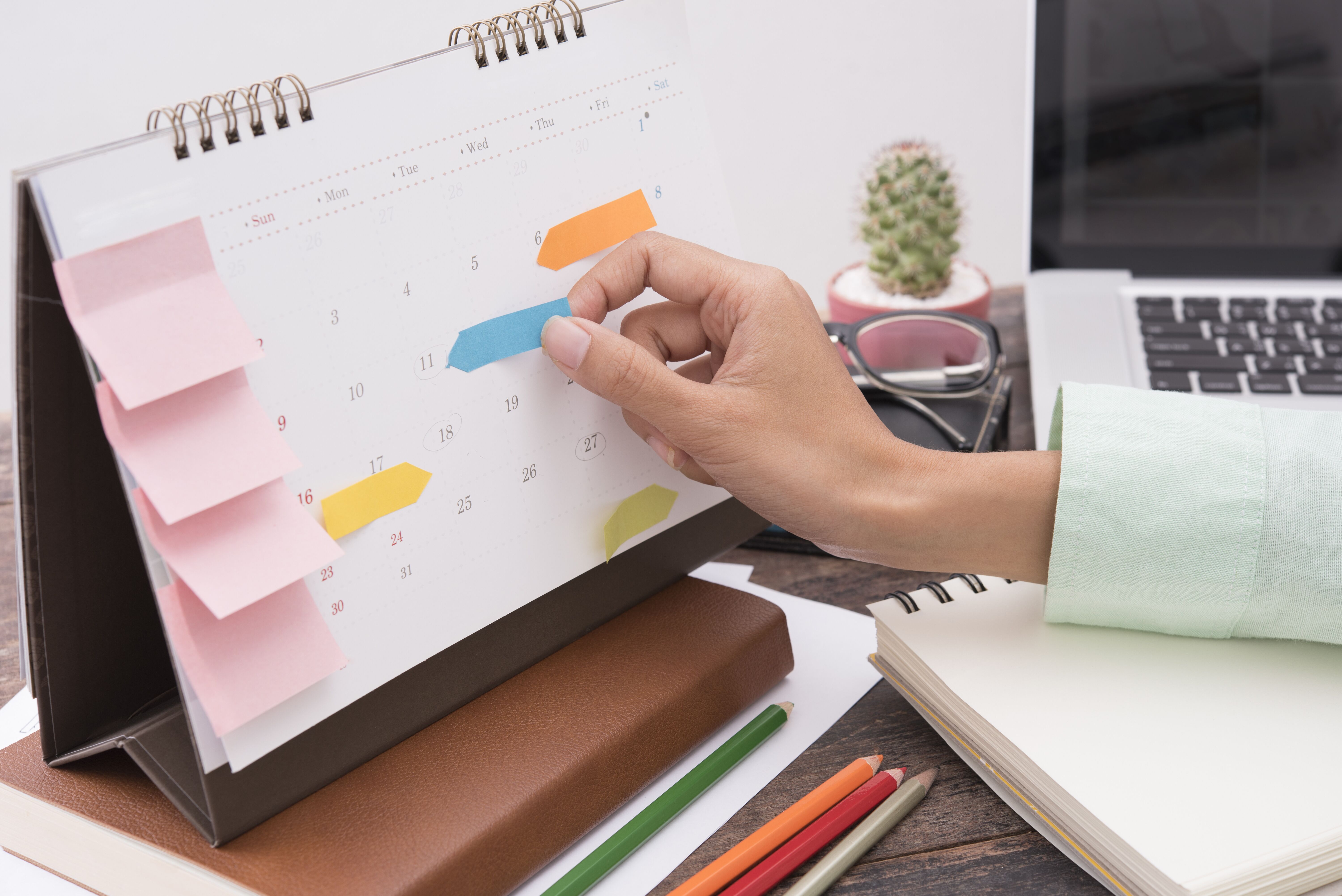 Efficient office routine - an individual in an office attaching markers to a calendar for organization