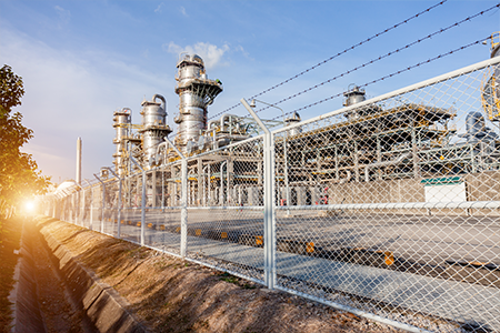 Secure perimeter view of a production site with chimneys, featuring a protective fence guarding the industrial facility.